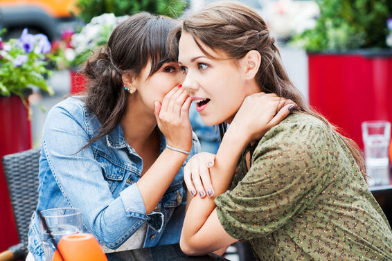 Two best friends sitting in a cafe whispering and gossiping